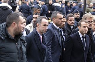 Macron, žluté vesty, muži v černém